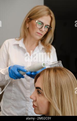 Doctor examines head skin of a young girl with special dermatology equipment system, hairloss and trichology concept Woman Analyzing Hair With Stock Photo