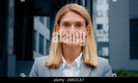 Close-up caucasian woman standing outdoors successful businesswoman professional lawyer corporate employee happy client smiling looks at camera posing Stock Photo