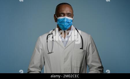 Close-up mature male doctor surgeon in protective mask looks at camera man experienced hospital worker posing in studio on gray background advertising Stock Photo