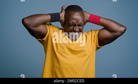 Close-up adult male athlete sportsman standing in studio on gray background angry annoyed anxious man suffering from loud noise covering ears with Stock Photo