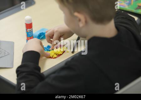 Shallow depth of field (selective focus) details with Ukrainian refugee children glueing Ukrainian heart shaped flags. Stock Photo