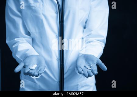 Cropped view of female Doctor holding in hands Pills to choose. Difficult Choice between drugs. Placebo drugs concept. Healthcare concept. Stock Photo