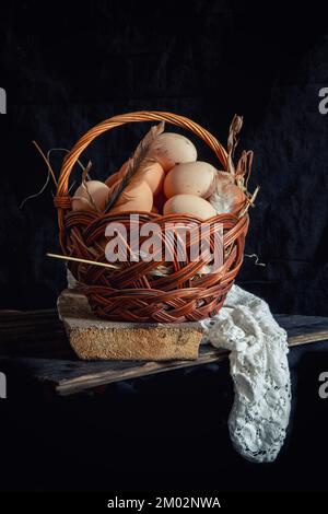 Chicken eggs in a wicker basket on a dark background. Stock Photo
