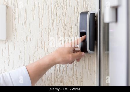Close-up photo. The man's finger presses the button of the black electronic doorbell with a camera on the wall of the house, office. Stock Photo