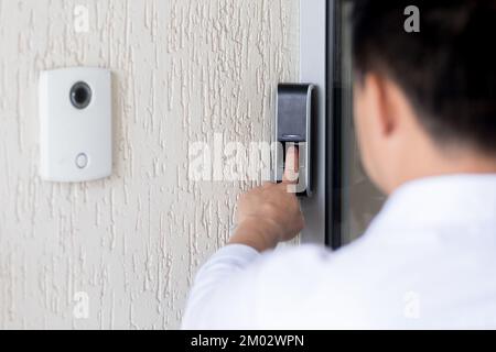 Close-up photo. A young man presses his finger on a black electronic doorbell in a building next to a white video camera. Delivery, guest, office. Stock Photo