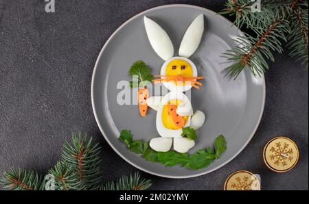 Funny rabbit made from boiled eggs, peeled carrots and arugula on gray plate. Creative food idea for kids, Top view, Flat lay Stock Photo