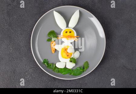 Funny rabbit made from boiled eggs, peeled carrots and arugula on gray plate. Creative food idea for kids Stock Photo