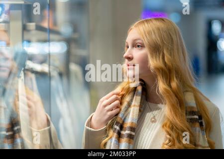 Shopping. A young girl looks at shop window, dreaming, makes purchases in a mall. Stock Photo