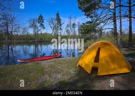 A tourist tent in the spring forest. Camp of tourists on the background of a forest river. Stock Photo