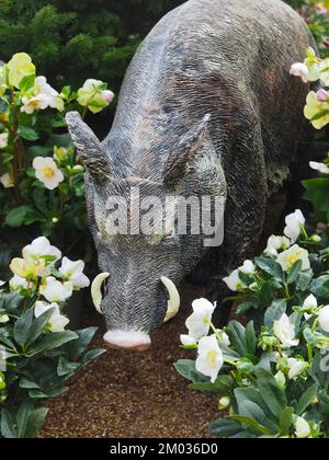 Sculpture of a wild boar in a garden with flowers Stock Photo