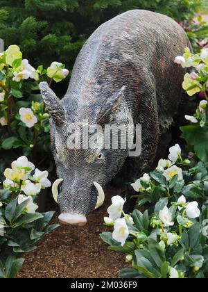 Sculpture of a wild boar in a garden with flowers Stock Photo