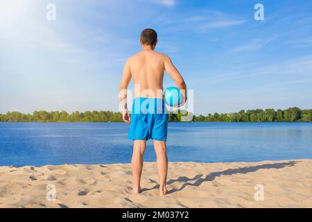 A man with a volleyball ball on the beach on a sunny day. The view from the back Stock Photo