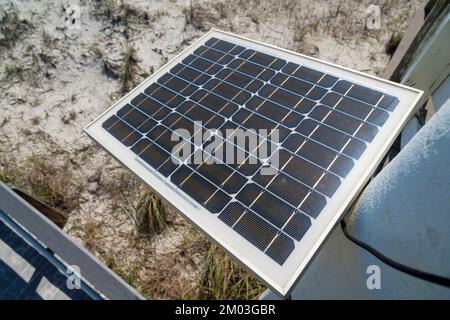 Close-up top view of a solar panel at Destin, Florida. Solar panel mounted on a wall with direct sunlight above the sandy ground with grasses. Stock Photo