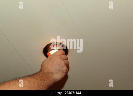 Installing a spot light, the hand inserts the lamp into the ceiling. Replacing a burned out incandescent bulb. Stock Photo