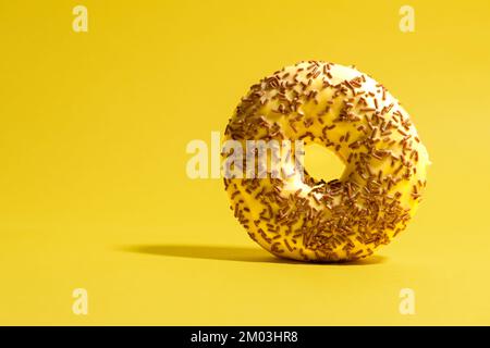 Yellow donut with chocolate crumbs on yellow background. Creative food background Stock Photo