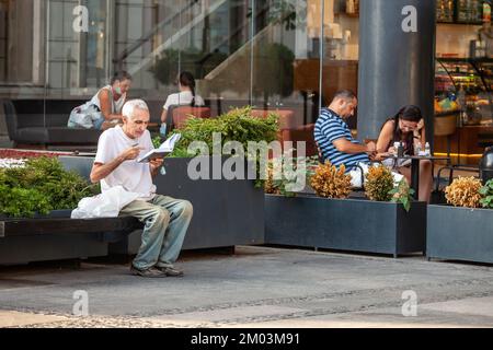 Picture of an old man sitting on a public bench reading a book outdoors in Belgrade, the biggest city of Serbia. Stock Photo