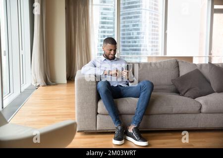 Cheerful African mobile phone user man resting on sofa Stock Photo