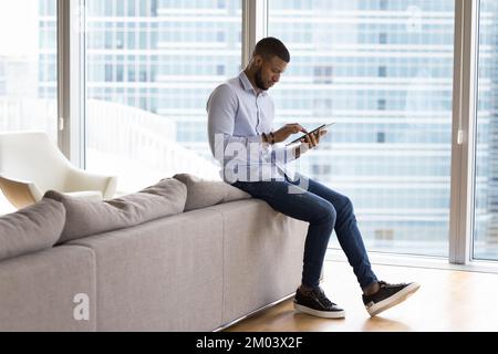 Focused millennial African tablet user man reading text on screen Stock Photo