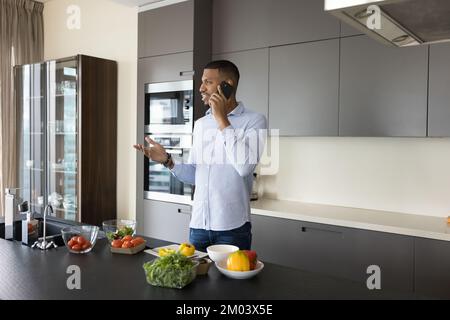 Positive young African chef guy making call on mobile phone Stock Photo