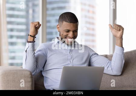 Cheerful happy young millennial Black business man looking at laptop Stock Photo