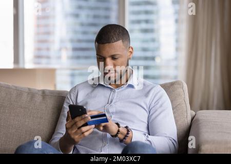 Focused mobile phone user man using credit card Stock Photo
