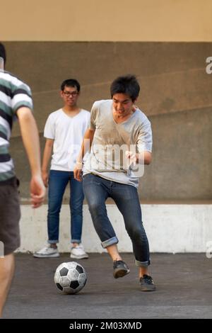 Showing off his mad skills. Three asian teenagers playing soccer in the street. Stock Photo