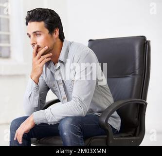 Something is weighing heavily on his mind. a handsome young sitting in a chair. Stock Photo