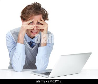 I am freaking out right here. A young man grimacing through his fingers while sitting next to his laptop. Stock Photo