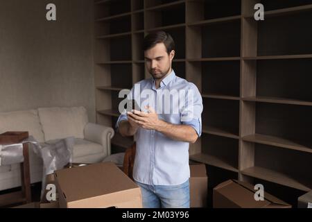 Focused home owner man using smartphone among cardboard boxes Stock Photo
