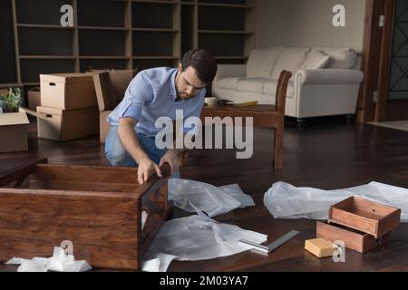 Focused apartment buyer man assembling furniture in new apartment Stock Photo