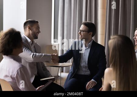 Two businessmen in formal suits shaking hands, start group meeting Stock Photo