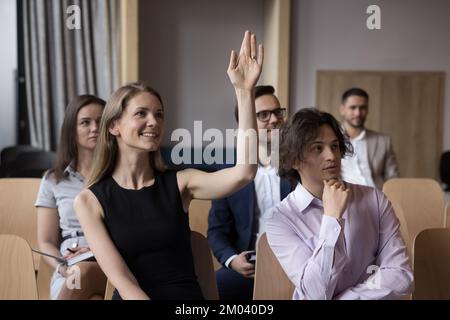 Smiling woman raising hand, asking question to business trainer Stock Photo