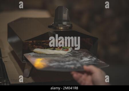 Unknown man putting a home made pizza in a practical table oven. Modern pizza being prepared at a party. Stock Photo