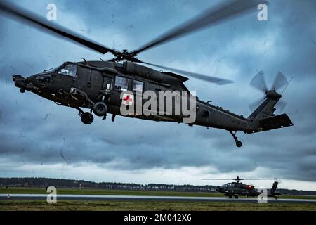 Powidz, Poland. 16th Nov, 2022. U.S. Soldiers assigned to Charlie Company, 2nd Battalion, 501st Aviation Regiment, Combat Aviation Brigade, 1st Armored Division (1AD CAB) operationally controlled by the 1st Infantry Division (1 ID) hovers a HH-60M Black Hawk helicopter during medical evacuation hoist training as a AH-64D Apache Longbow drives across the taxiway at the 33rd Air Base in Powidz, Poland, Nov. 16, 2022. The 1AD CAB is among other units assigned to the 1 ID, proudly working alongside NATO allies and regional security partners to provide combat-credible forces to V Corps, Americ Stock Photo