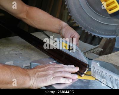adjusting the size when cutting a wooden plinth on the base of a miter saw, working with a wooden material on a circular saw in a carpenter's workshop Stock Photo