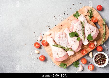 Raw chicken legs with seasonings and vegetables on wooden cutting board over light gray concrete background. Chicken drumsticks ready to cook. Organic Stock Photo