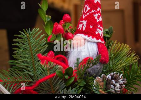 Cute gnome toy on Christmas tree. Small dwarf doll in red hat. Santa Claus doll on Christmas market. Christmas market. Christmas decor on pine tree. Stock Photo