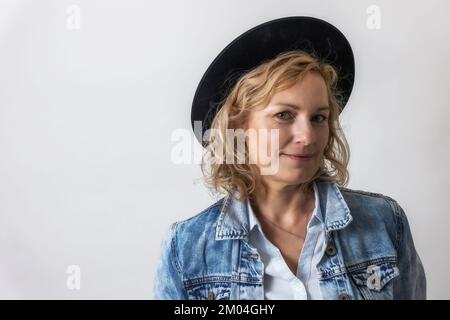 Portrait of  smiling  middle age woman with  black hat on the light background. Stock Photo