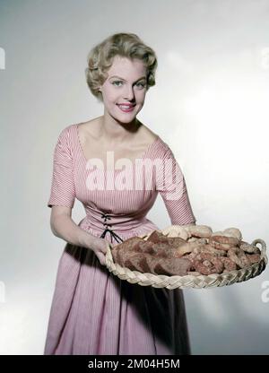 In the 1950s. A woman in a patterned dress is holding a tray with freshly baked cookies and buns. Sweden 1958 Stock Photo