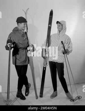 Winter clothes  in the 1950s. A young man and woman is wearing the typical 1950s winter sports clothes.  Dressed in a practical wind jacket, ski pants and with a pair of skis and poles.   Sweden 1959. Conard ref 3933 Stock Photo