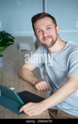 Attractive caucasian male freelancer or entrepreneur concept. Successful bearded man using tablet computer for business sitting at home office. High quality vertical photo Stock Photo