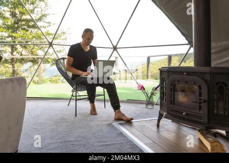 a man works on a laptop in a dome tent Stock Photo
