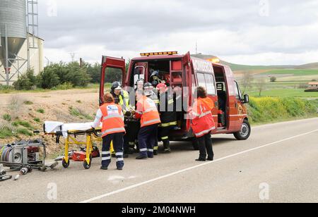 Fire van on a road next to a group of paramedics and firefighters who are treating an injured person from a traffic accident. Stock Photo