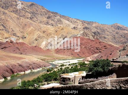 The Hari River (Harirud) near Chisht-e-Sharif in Herat Province, Afghanistan. The river flows through colorful mountain scenery past a farm with trees Stock Photo