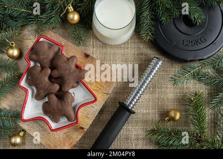 Chocolate gingerbread Christmas cookies, gym dumbbells weight plate, glass of milk for Santa Claus. Winter fitness diet, workout dieting concept. Stock Photo