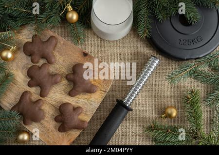 Chocolate gingerbread Christmas cookies, dumbbells weight plate, glass of milk for Santa Claus. Fitness winter diet, gym workout, dieting concept. Stock Photo