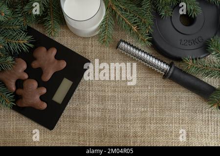 Gingerbread Christmas cookies on scale, gym dumbbells barbell weight plate, glass of milk for Santa Claus. Winter diet composition with copy space. Stock Photo