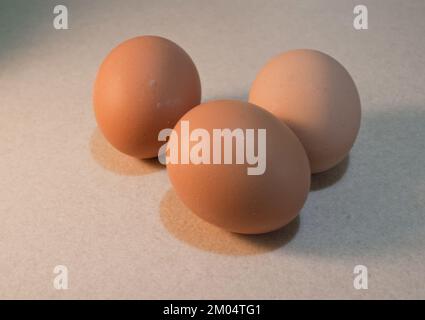 Three Brown Eggs Resting on a Beige Textured Surface Stock Photo