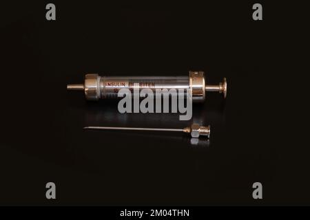 An old insulin syringe made of steel and glass with a needle on blck backgrount Stock Photo