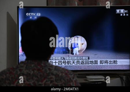 FUYANG, CHINA - DECEMBER 4, 2022 - Citizens watch a live TV broadcast of the re-entry module of the Shenzhou 14 manned spacecraft landing at Dongfeng Stock Photo